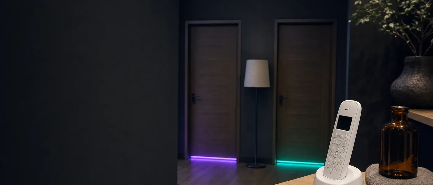 A salon phone on a reception ledge in front of two treatment room doors, one lit violet and one lit teal
