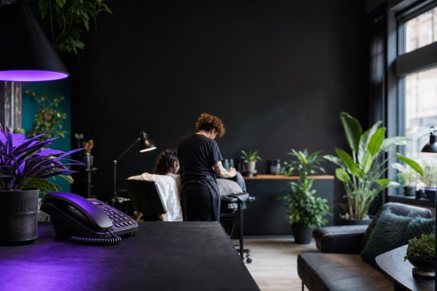 A stylist working with a client at the back of a plant-filled salon while the desk phone sits ignored in the foreground.